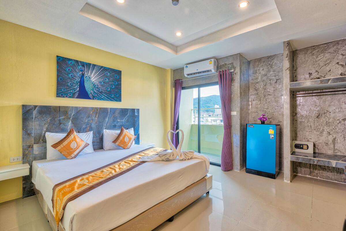 Une chambre d’hôtel avec un grand lit, un tableau représentant un paon, un minibar et une vue sur la ville.