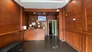 A reception area with a wooden reception desk, a bench, and a television mounted on the wall. - TJ PATONG HOTEL - Prime Location by OTOP Market & Sea (Patong)