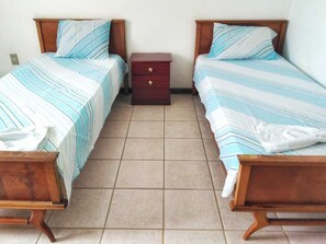 A room with two wooden beds with striped bedding, a small wooden nightstand, and tiled flooring. - Casa Sao Jose (Salvador)