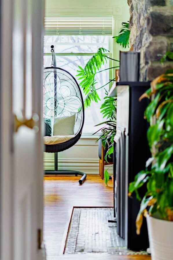 Een gezellige woonkamer met een hangstoel, een open haard en verschillende potplanten.