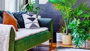 A modern living room with a green sofa, multiple potted plants, and a staircase in the background. - Short North/Downtown | Near High St | Walk to Convention Center | 5,800+ Reviews (Columbus)
