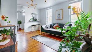 A modern living room with a green sofa, wooden flooring, and multiple ceiling lights. - Short North/Downtown | Near High St | Walk to Convention Center | 5,800+ Reviews (Columbus)