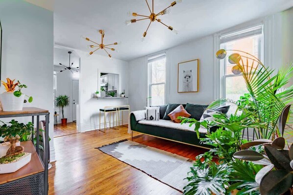 Un salon moderne avec un canapé vert, un plancher en bois et de nombreux luminaires au plafond.