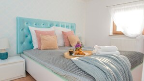 A neatly made bed with a tufted headboard, multiple pillows, a tray with croissants and a drink, and a window with sheer curtains.