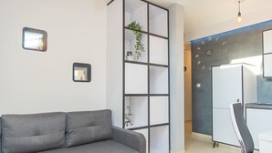A modern room with a grey sofa, a tall shelving unit with a plant, and a wall clock.