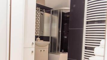 Un bagno moderno con un mobile lavabo bianco, cabina doccia in vetro e parete rivestita in piastrelle nere.
