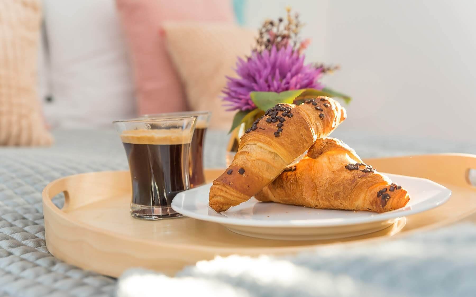 A tray with croissants and a cup of coffee on a bed.
