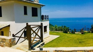 A white building with a stone chimney, a wooden gate, and a view of the sea. - Villa Mylopotamos (Zagora-Mouresi)