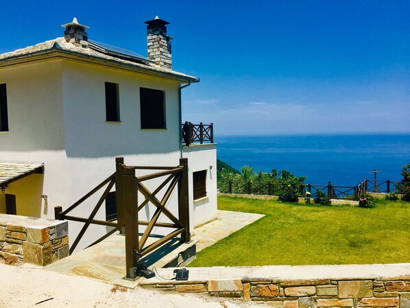 Edifici blanc amb un camí de pedra, una porta de fusta i vistes al mar.