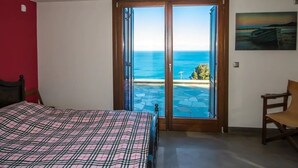 A bedroom with a bed, a chair, and a view of the sea through a glass door. - Villa Mylopotamos (Zagora-Mouresi)