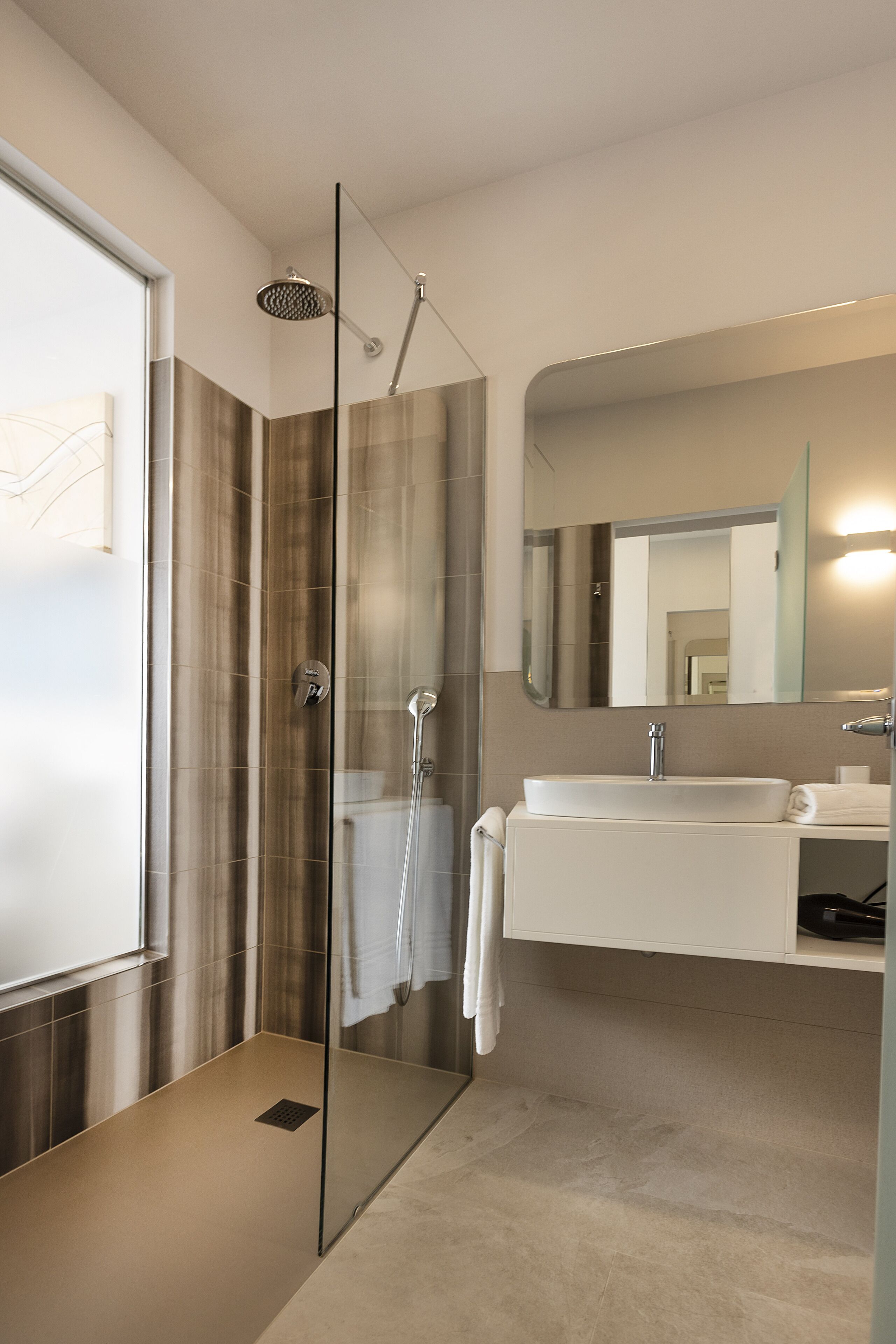 Een moderne badkamer met een douchecabine van glas, een wit wastafelmeubel en een grote spiegel.
