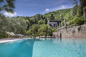 A swimming pool with lounge chairs, a stone wall, and a building with a stone facade. - Hotel Livia (Gargnano)