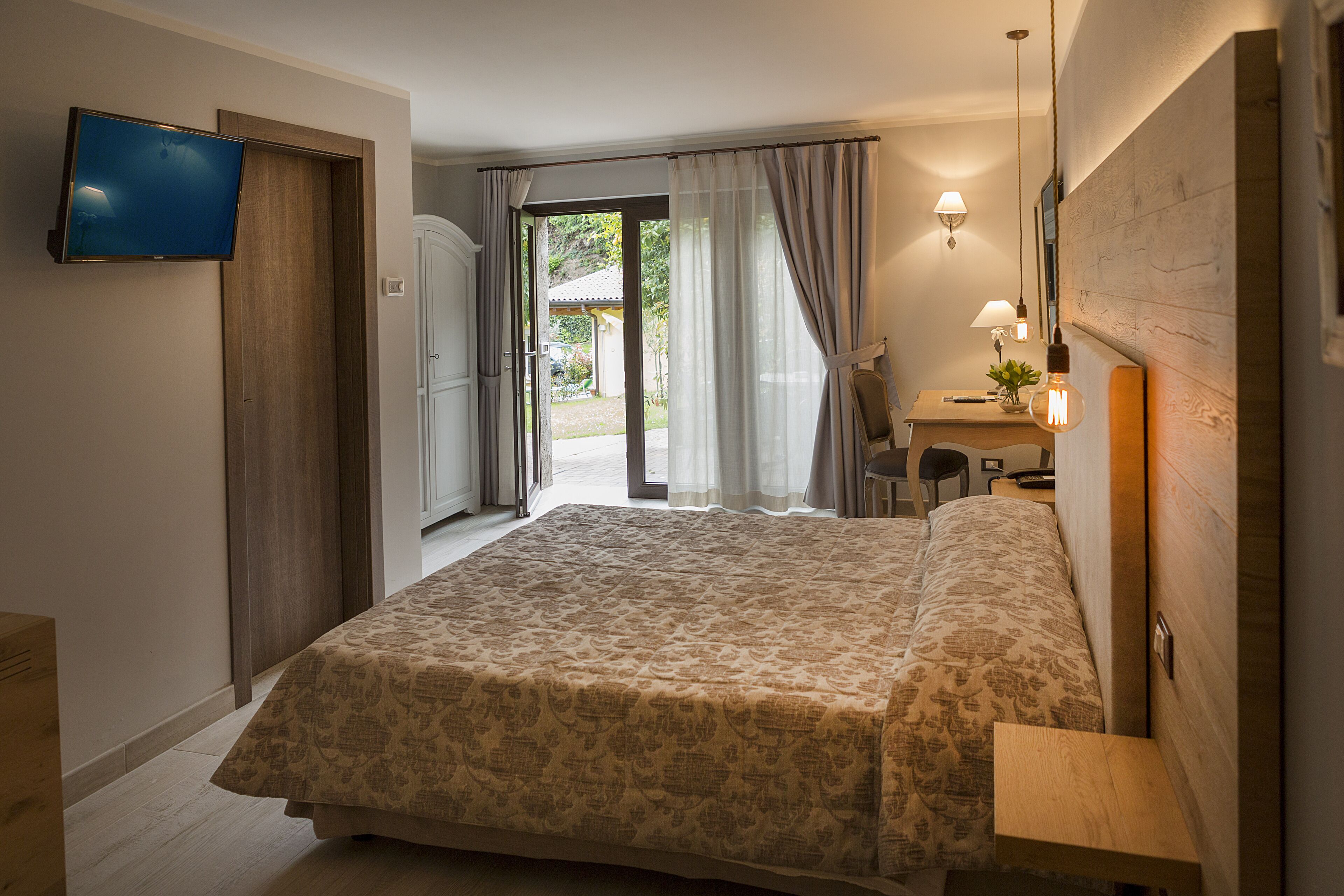 Habitación de hotel con cama, escritorio, silla, televisión y puerta corredera al exterior.