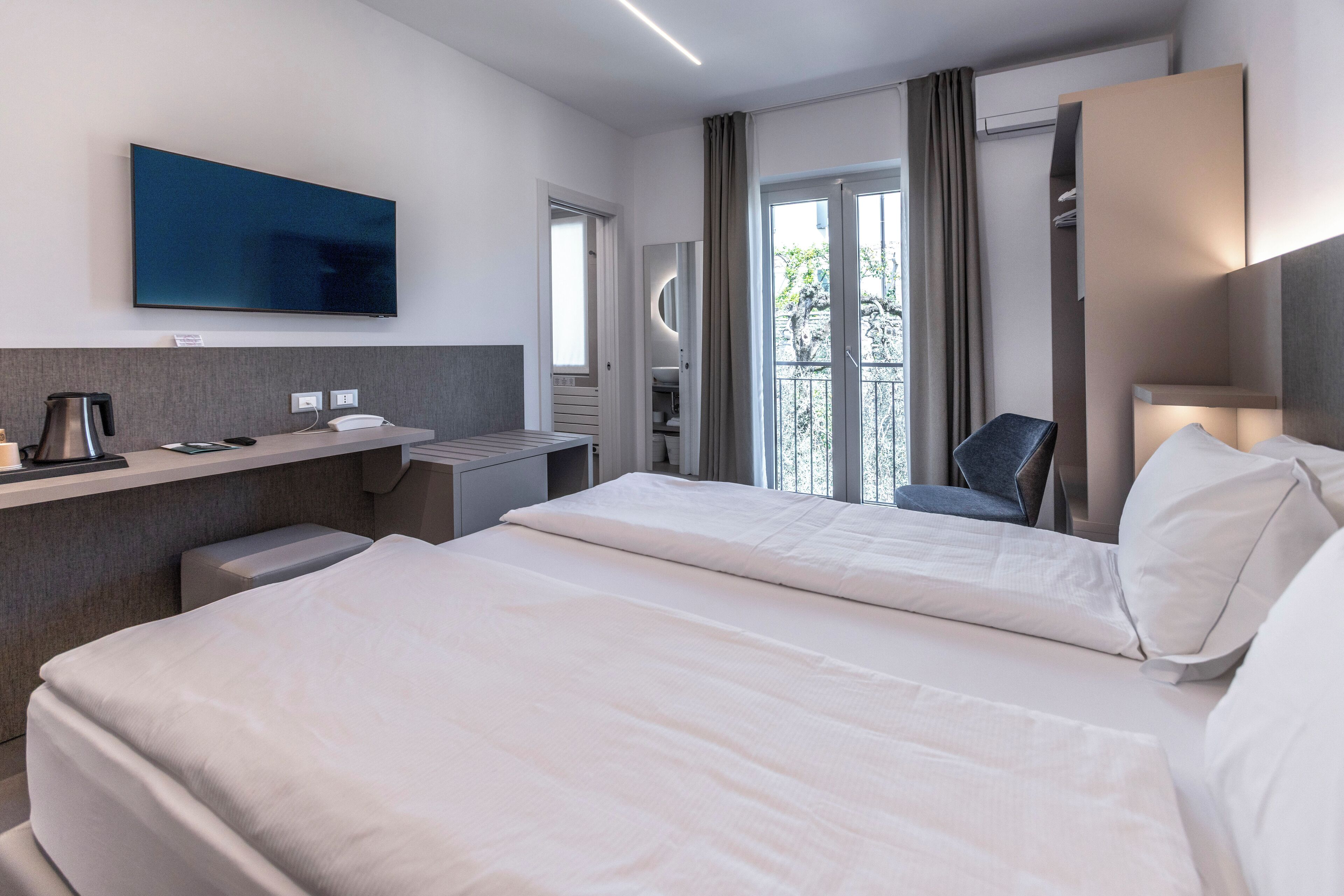 Quarto de hotel moderno com duas camas, uma televisão de tela plana, uma escrivaninha com cafeteira e vista para o exterior.