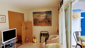 A living room with a television on a stand, a wicker chair, a sofa, a painting on the wall, and a blue door. - Appt COCOONING, Nice Terrace + BIKES 🤩PROXIMITY OF 2 BEAUTIFUL BEACHES 🏖️et PORT (La Baule)