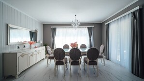 A dining room with a marble floor, a chandelier, a dining table with six chairs, a cabinet with decorative handles, and a large window with curtains. - Luxury villa Tori in Imotski, pool (Lokvicici)