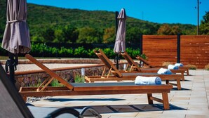 A row of wooden lounge chairs with towels, set on a tiled patio with a stone wall and wooden fence in the background. - Luxury villa Tori in Imotski, pool (Lokvicici)