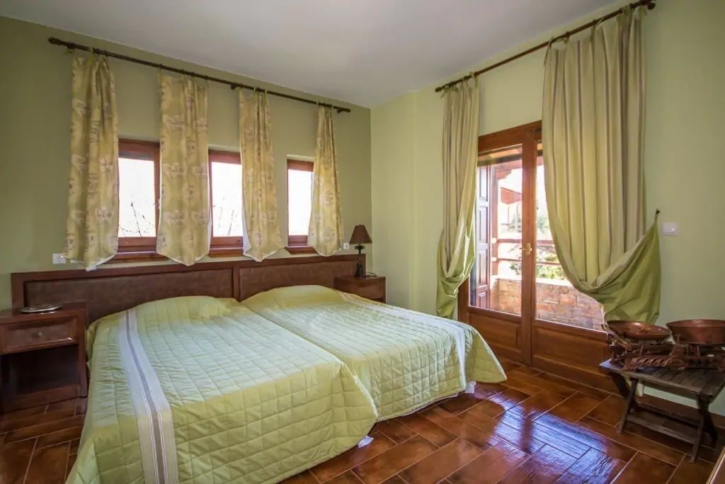 Un lit double avec une couvre-lit matelassé, deux tables de chevet, une tête de lit en bois et une fenêtre avec des rideaux.