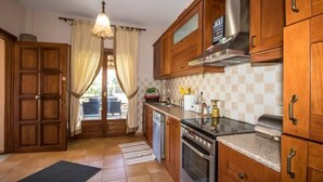 A kitchen with wooden cabinets, a stainless steel range hood, and a tiled backsplash. - Villa Helios (South Pelion)