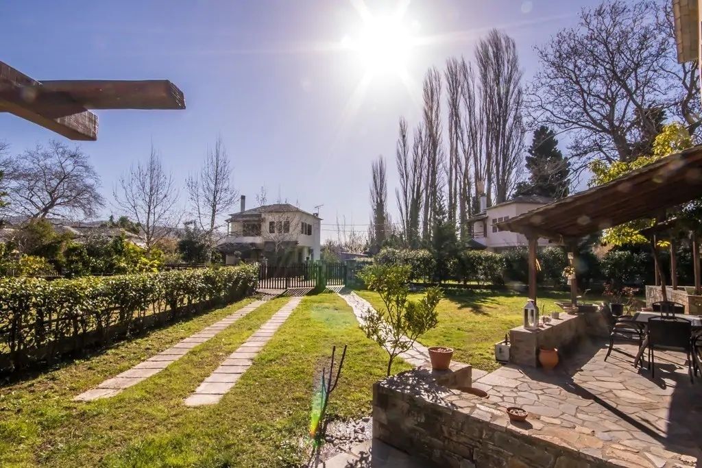 Un jardín con un sendero de piedra, un árbol pequeño y un patio con mobiliario exterior.