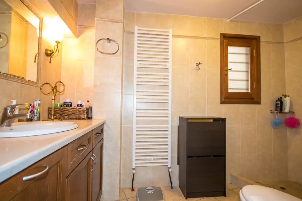 Ein Badezimmer mit Waschbecken, Spiegel, Handtuchhalter, Heizung und Toilette.