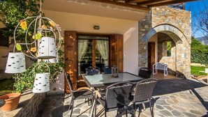 An outdoor patio with stone flooring, wicker furniture, and hanging birdcages. - Villa Helios (South Pelion)