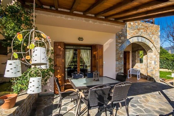 An outdoor patio with stone flooring, wicker furniture, and hanging birdcages.