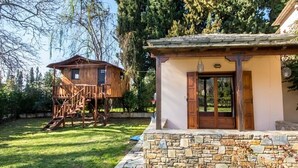 A wooden cabin with a stone foundation, a wooden deck, and a large window. - Villa Helios (South Pelion)