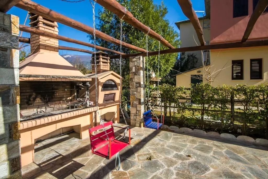Une terrasse extérieure avec un sol en pierre, un barbecue en briques et une balançoire.
