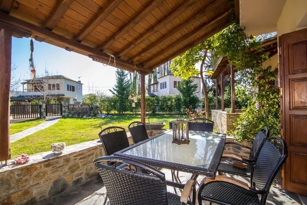 An outdoor patio with a glass-top table and wicker chairs, surrounded by stone walls and greenery.