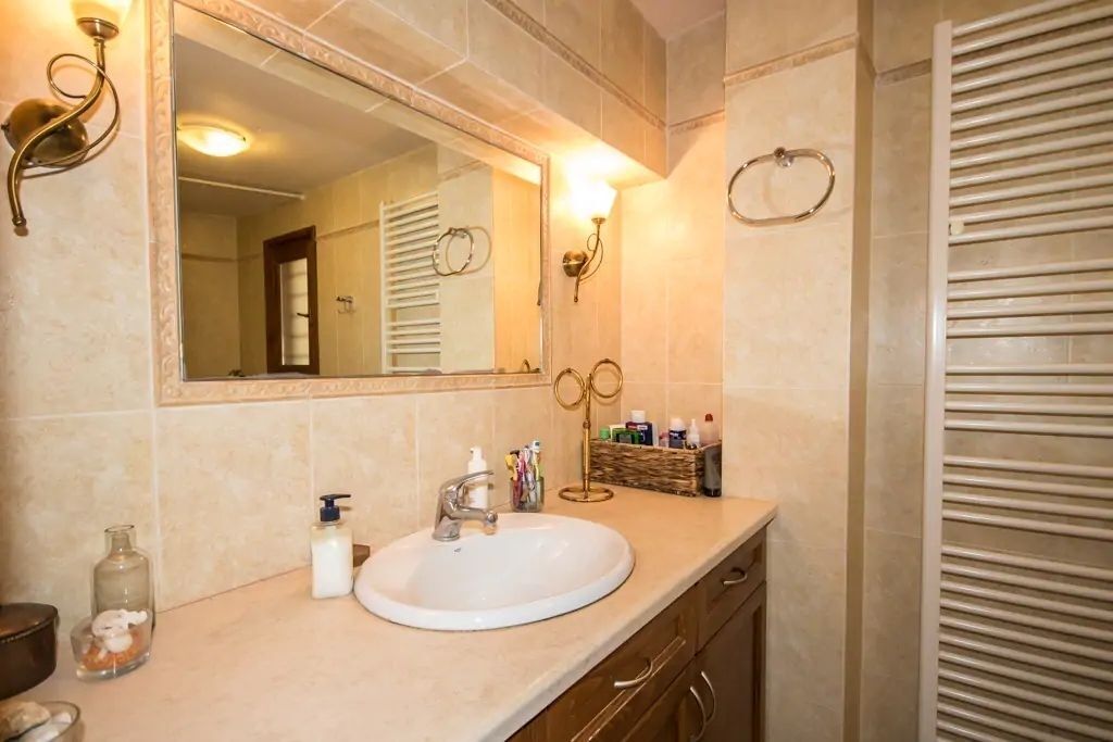 Un baño con un lavabo blanco, un espejo grande y un perchero para toallas.