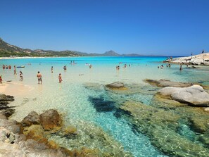 A beach with clear turquoise water, rocky formations, and people swimming and sunbathing. - Nice apartment in villa for 6 people with A/C, TV, terrace and pets allowed (Castiadas)