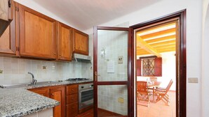 A kitchen with wooden cabinets, a granite countertop, and a tiled backsplash. - Cosy apartment in villa for 6 people with A/C, TV, terrace and pets allowed (Castiadas)
