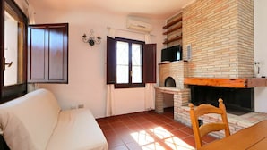 A room with a brick fireplace, a sofa, a dining table, and a TV mounted on the wall. - Cosy apartment in villa for 6 people with A/C, TV, terrace and pets allowed (Castiadas)