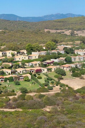 A hillside village with stone buildings, green gardens, and a clear view of distant mountains.