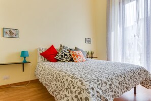 A bedroom with a bed, a nightstand, a lamp, and two wall-mounted pictures.