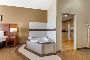 Un baño de hotel con una bañera grande, zona de ducha y una mesita de noche de madera con lámpara.