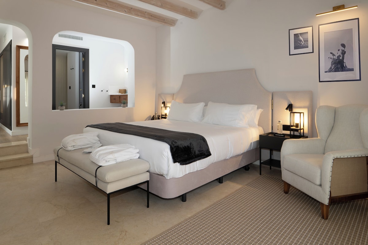 A bedroom with a bed, a chair, a nightstand, and a mirror.