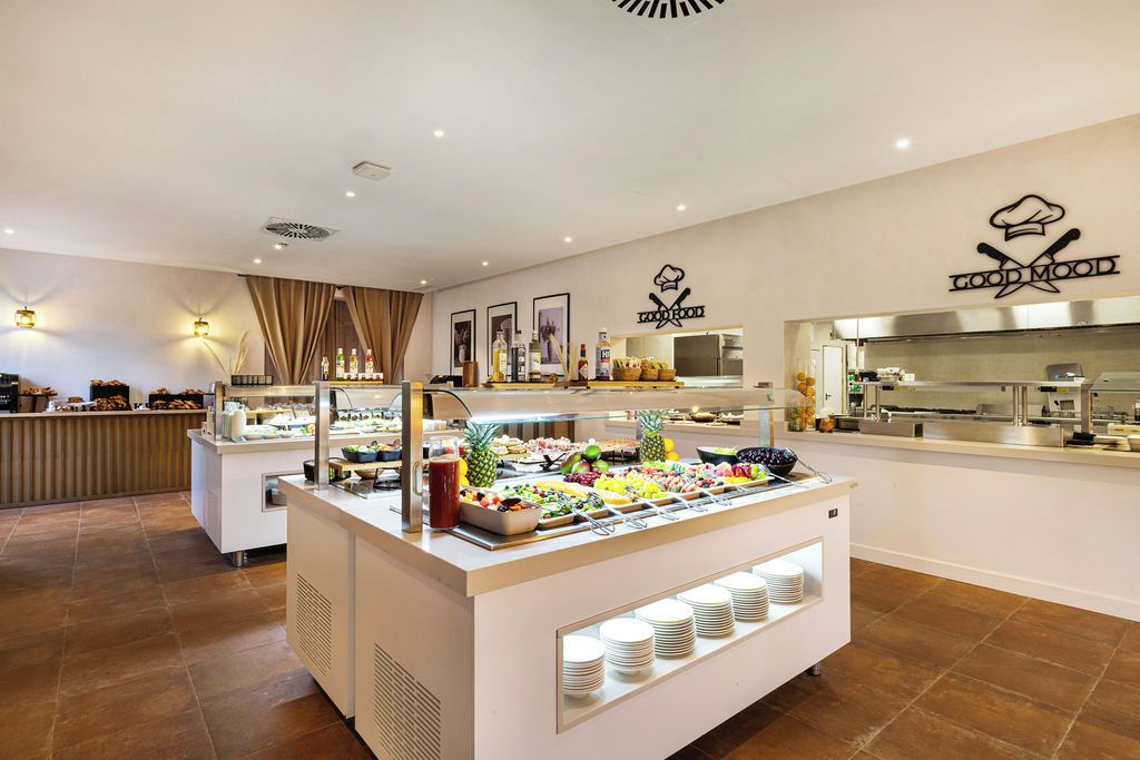 Een buffetgedeelte met verschillende keuzes, een keuken op de achtergrond, en een bordje met de tekst 'GOOD MOOD'.