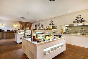 Zona de buffet con diversas opciones de comida, una cocina al fondo y un letrero que dice 'GOOD MOOD'.