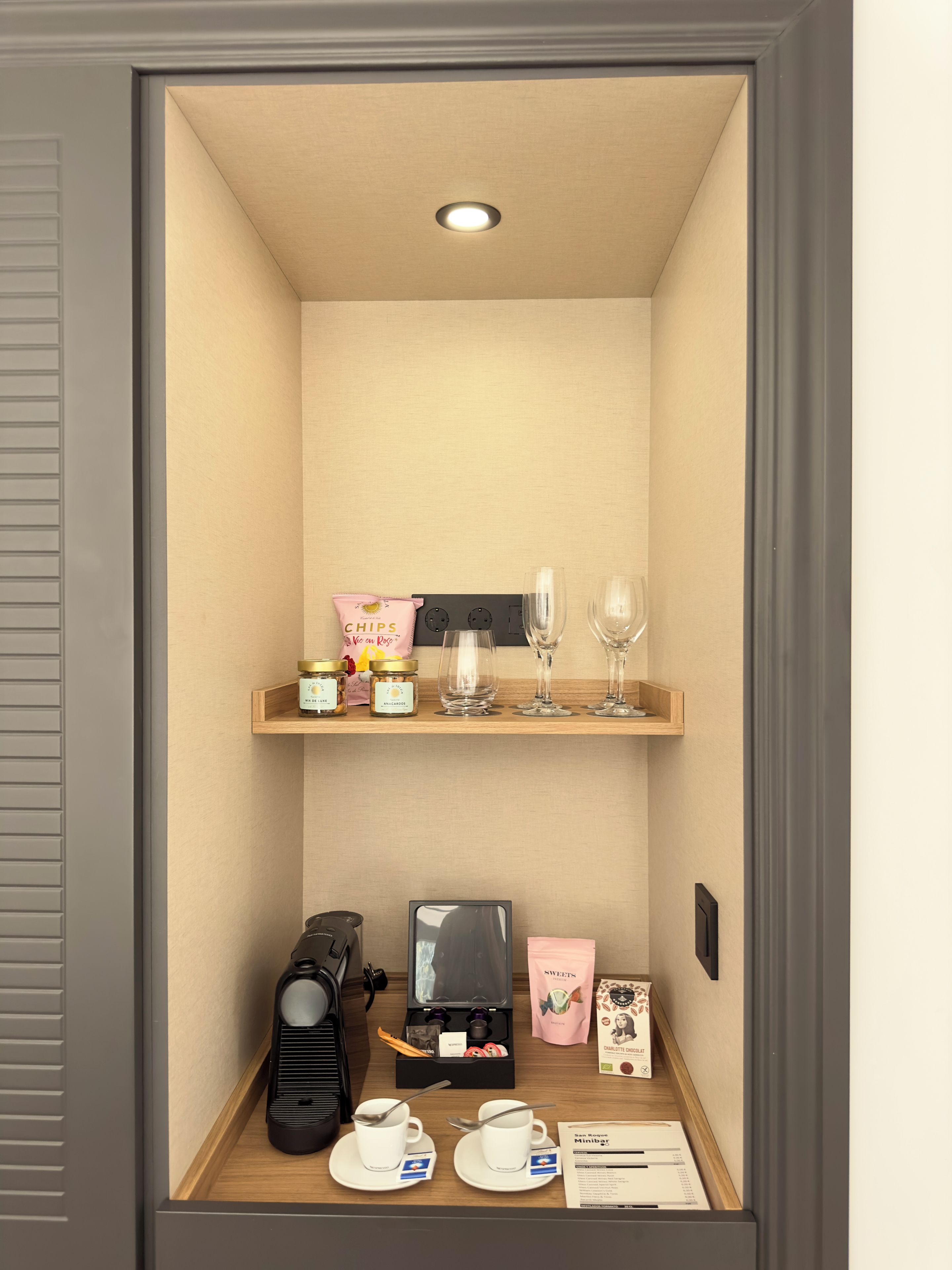 Un minibar compacto con aperitivos, vasos, una cafetera y un televisor pequeño.
