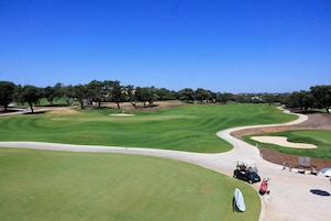Un campo de golf con cielo despejado, árboles y un carrito de golf.