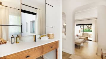 Un baño moderno con un espejo grande, tocador de madera y vista a un área de estar con sofá y sillones.