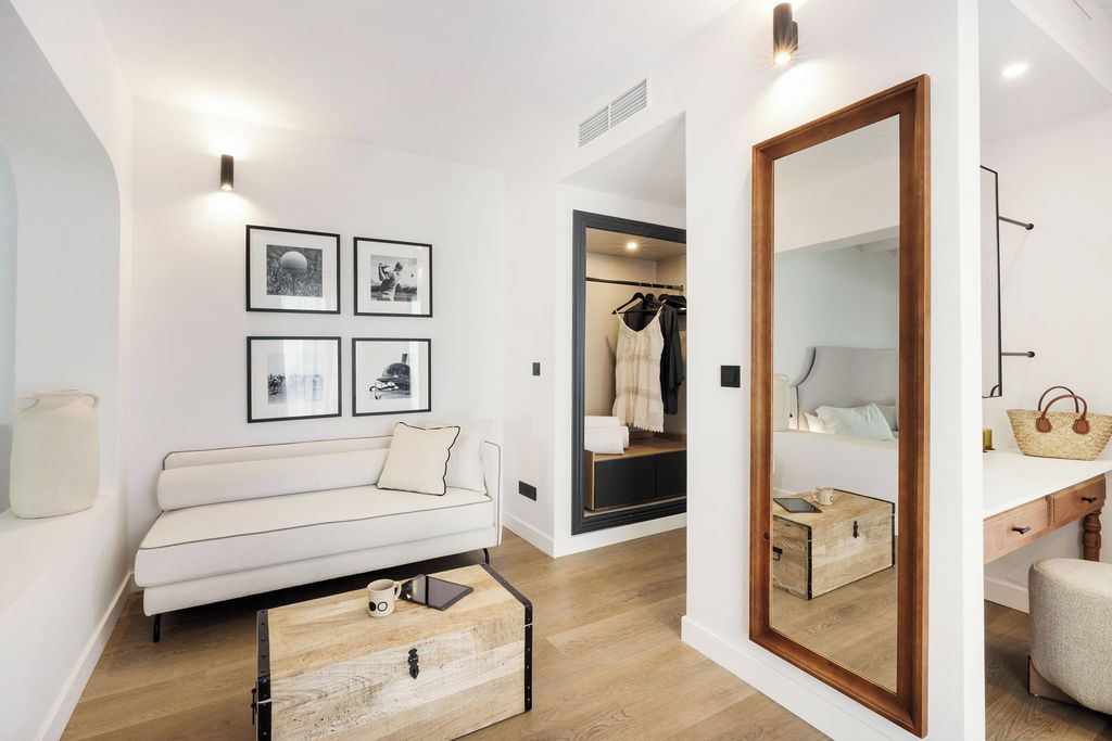 Un interior moderno con un sofá, un cofre de madera, cuadros enmarcados, un espejo y un vestidor.
