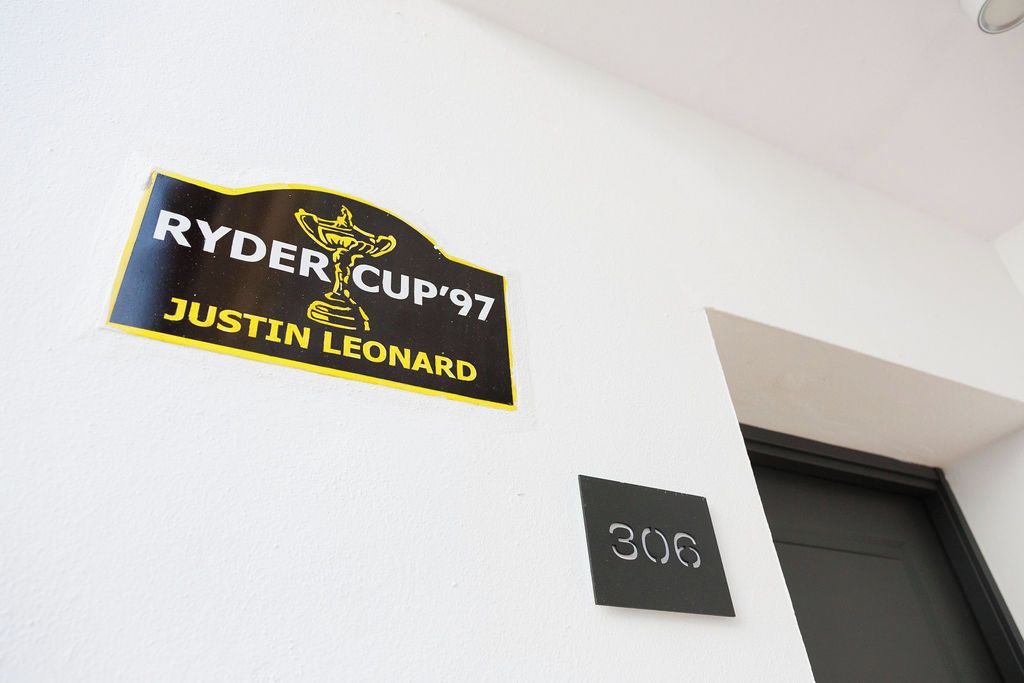Una pared con un letrero que dice 'RYDER CUP '97 JUSTIN LEONARD' y un letrero más pequeño con el número '306'.
