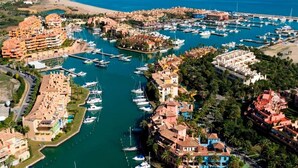 Vista aérea de un pueblo costero con un puerto deportivo, propiedades frente a la playa y edificios residenciales densos.