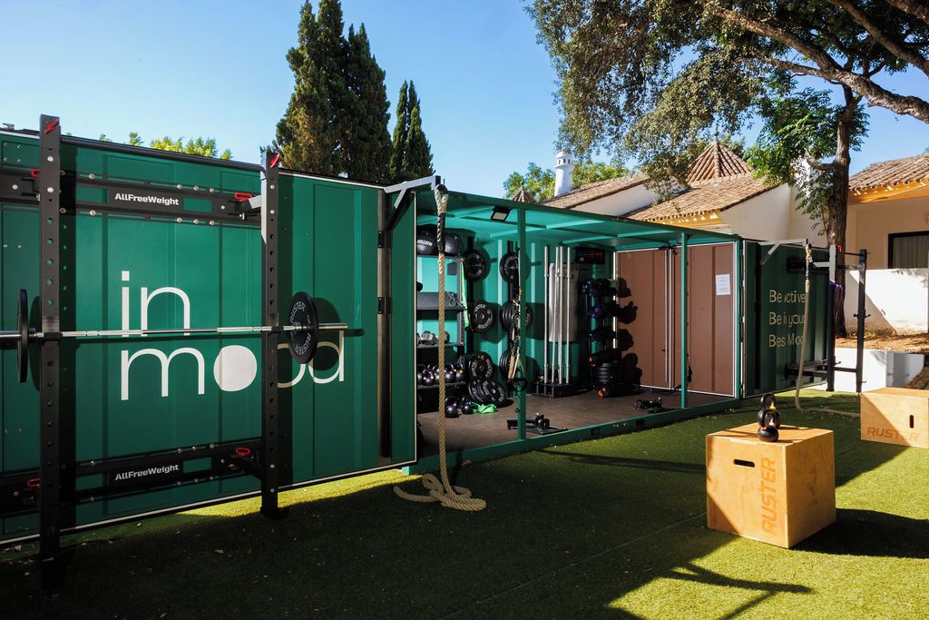 Un gimnasio con un contenedor verde etiquetado 'in mo' y equipo de levantamiento de pesas.