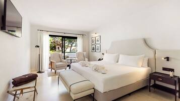 A hotel room with a large bed, a bench, a bedside table, a flat-screen TV, and a window with curtains.