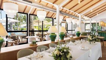 Un restaurante con mesas dispuestas para comer, grandes ventanales y plantas de interior.