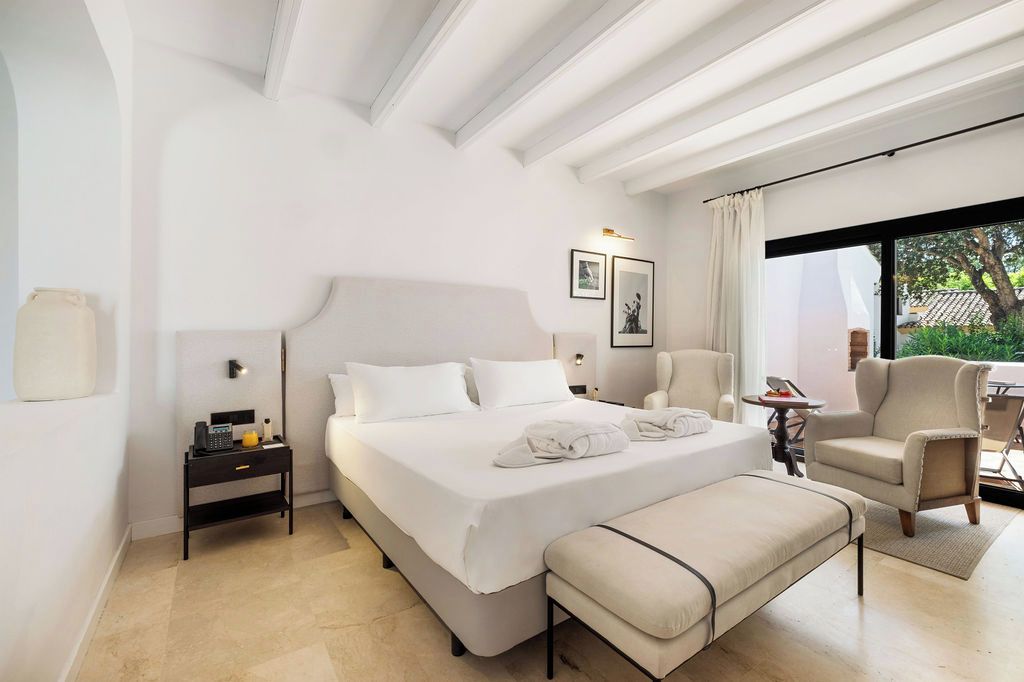 Habitación de hotel moderna con una cama grande, una mesita de noche, una silla y vistas al exterior.